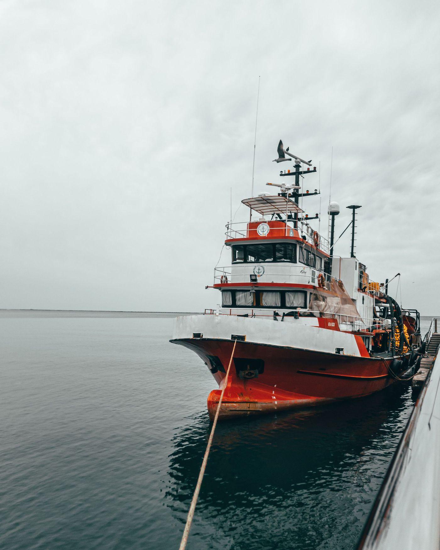 A red and white survey vessel tied up alongside a pier